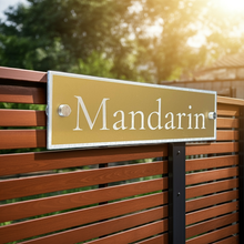 Gold aluminium sign with stainless steel fixings, holding the sign off the wooden fence with a natural background
