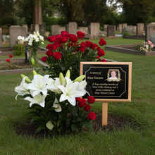 Floral arrangement with red and white flowers and a memorial plaque in a cemetery.