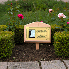 Memorial plaque with a cross and text in a garden setting with flowers.
