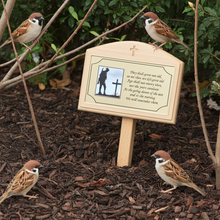 Small wooden plaque with a photo and text on a garden ground with sparrows around.