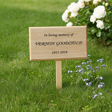 Wooden memorial sign on grass with flowers in the background
