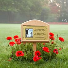 Memorial plaque with a silhouette of a person and a cross, surrounded by red poppies on a grassy field.