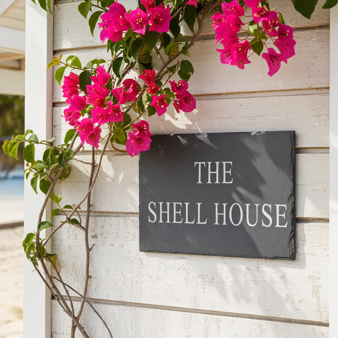 Pink flowers with a sign reading 'The Shell House' on a wooden wall.