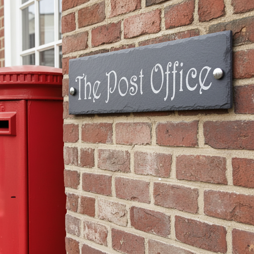 Slate sign reading 'The Post Office' on a brick wall next to a red postbox.