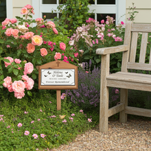 Memorial garden with pink flowers, a wooden bench, and a plaque.
