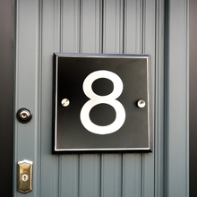 House number '8' on a black plaque attached to a gray door.