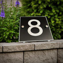 Black plaque with the number '8' on a stone ledge with greenery in the background