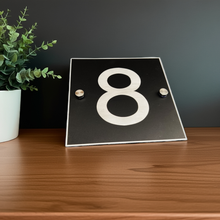 Black plaque with the number '8' on a wooden surface next to a plant.