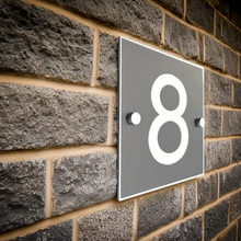House number '8' on a gray rectangular plate attached to a brick wall.