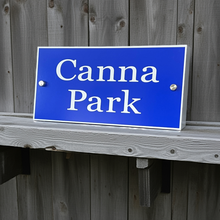 Blue sign with 'Canna Park' text mounted on a wooden fence