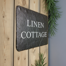 Slate sign with 'Linen Cottage' text on a wooden surface with greenery