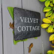 Slate sign with 'Velvet Cottage' text on a wooden surface with leaves.