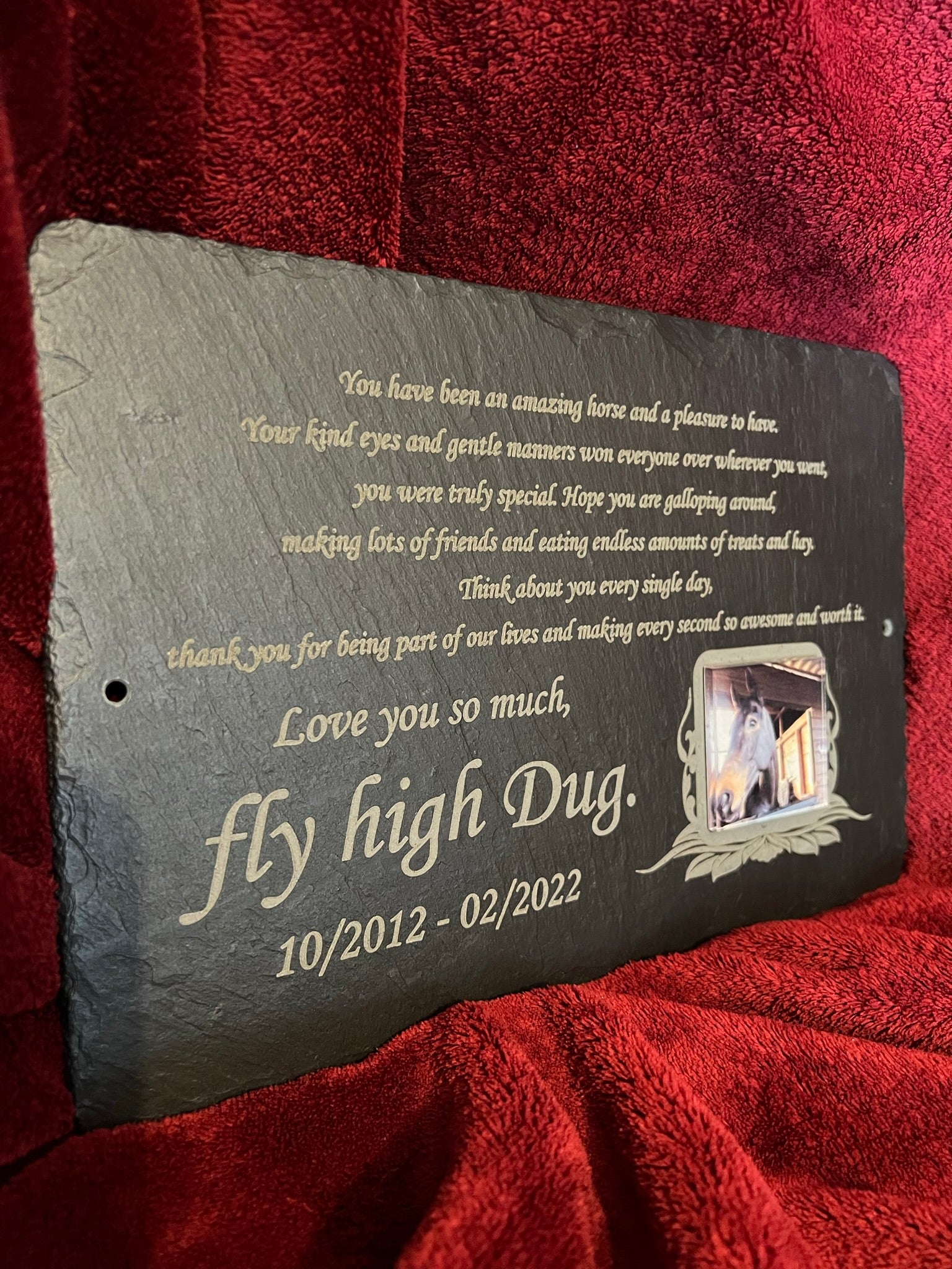 A personalized dark gray slate memorial plaque with engraved gold text and a small photo frame, displayed on a red textured fabric background.