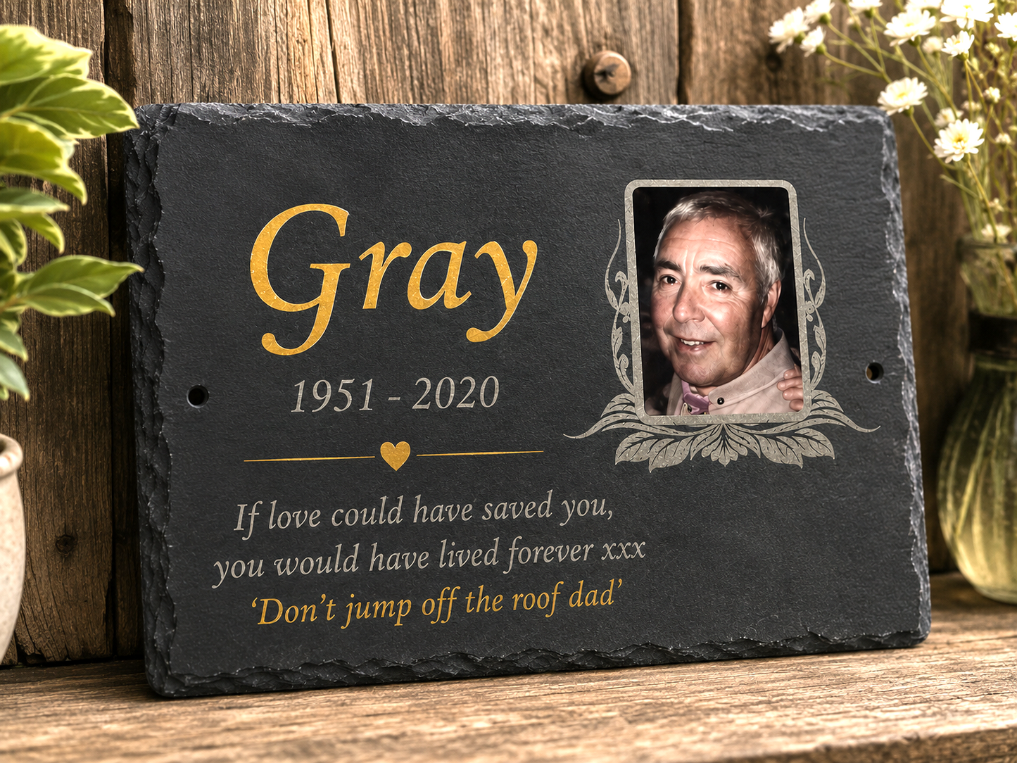 Personalized black slate memorial plaque with a photo of a man, the name Gray in gold, dates 1951-2020, and a remembrance quote, displayed on a wooden surface.
