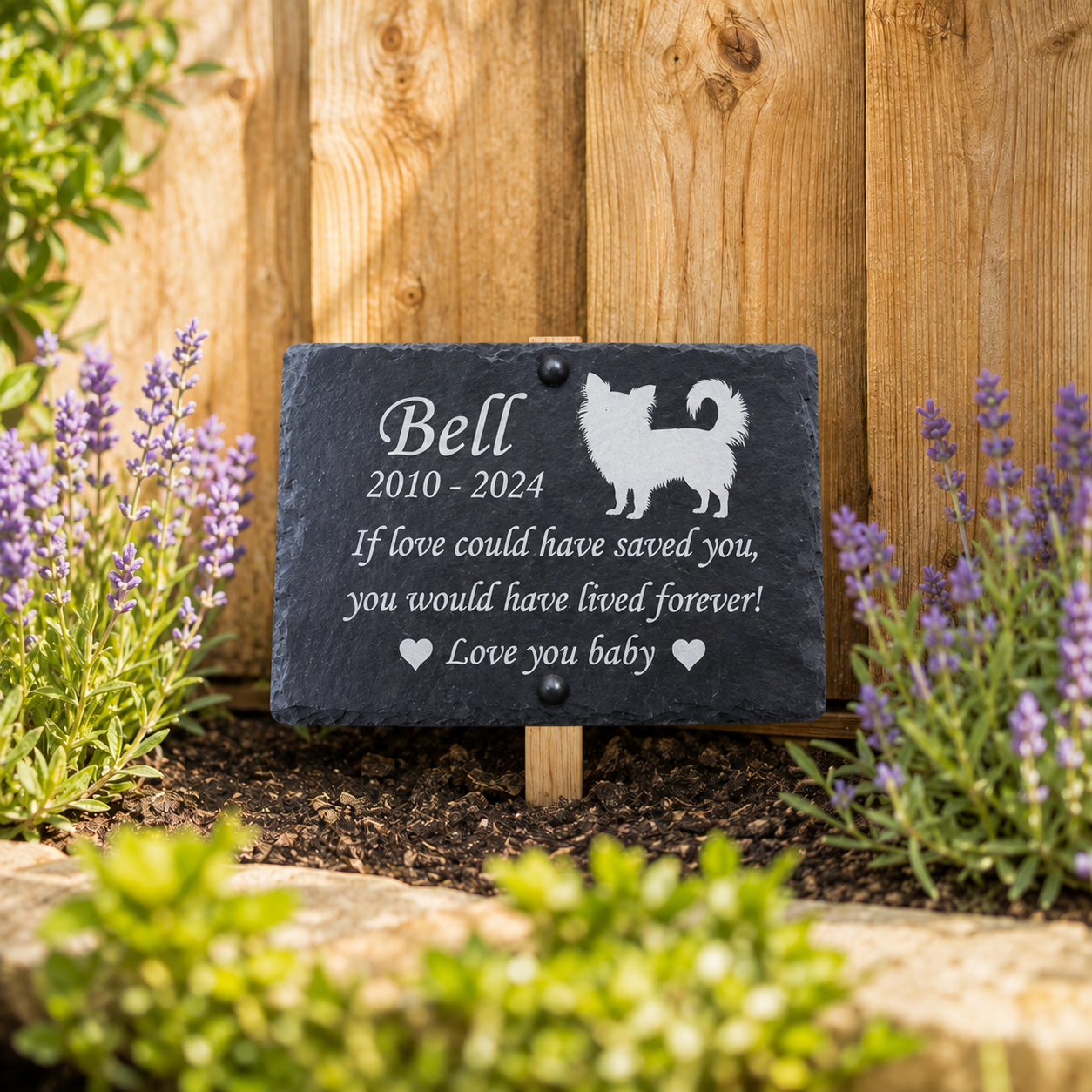 Personalized black slate pet memorial garden plaque with engraved white text and silhouette, mounted on a wooden stake in a garden bed with lavender flowers and a wooden fence background.