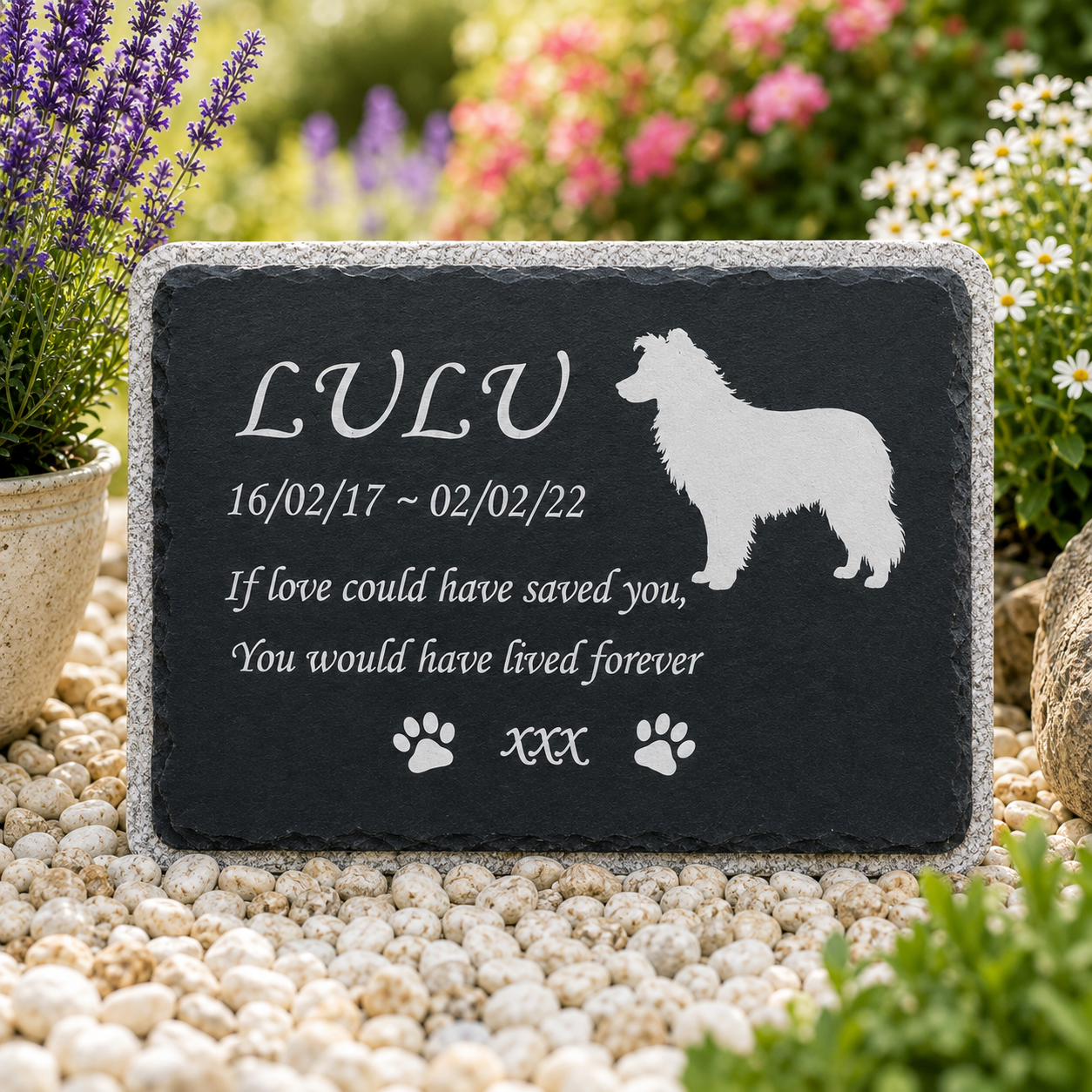 Personalized black slate pet memorial garden stone with engraved white text, dog silhouette, and paw prints, displayed on white pebbles in a garden setting.
