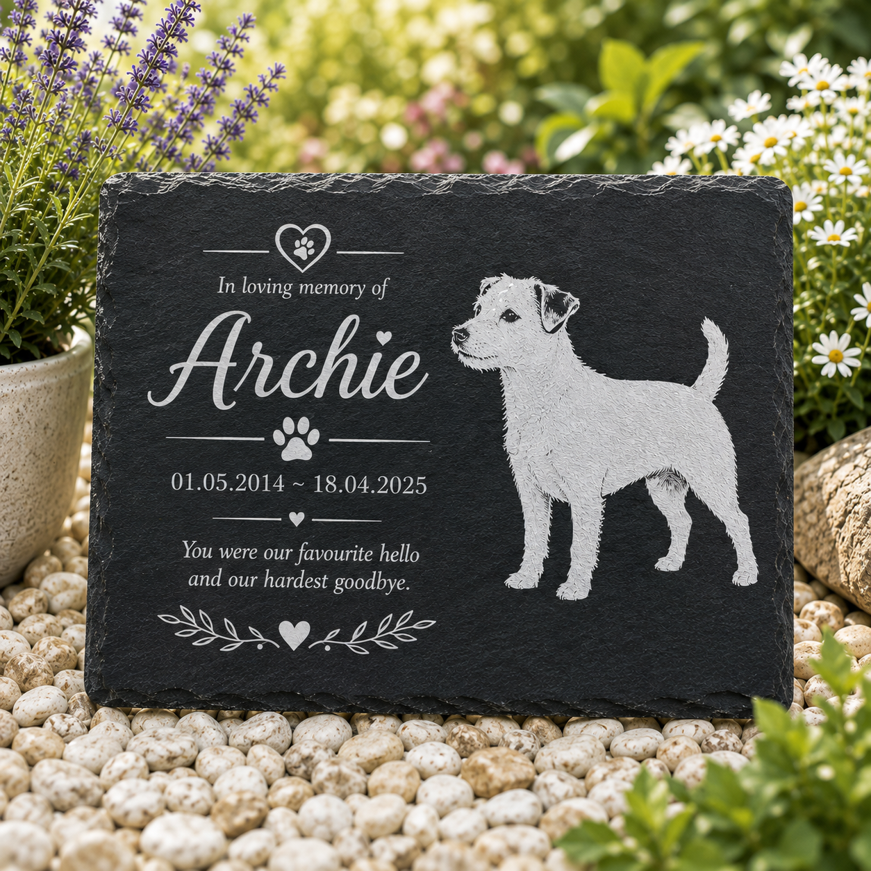 Personalized black slate pet memorial garden stone engraved with a dog silhouette, paw print, and the text 'In loving memory of Archie' with dates and remembrance message, displayed on white pebbles with plants in the background.