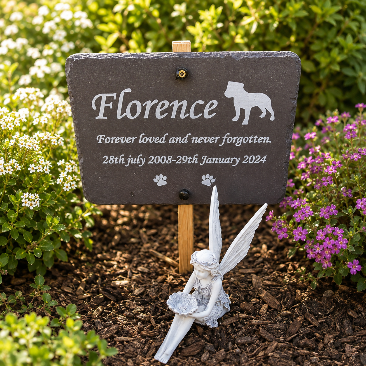 Personalized pet memorial garden sign on a wooden stake, featuring a dark slate plaque engraved with the name 'Florence' and a dog silhouette, surrounded by a small angel figurine in a garden setting.
