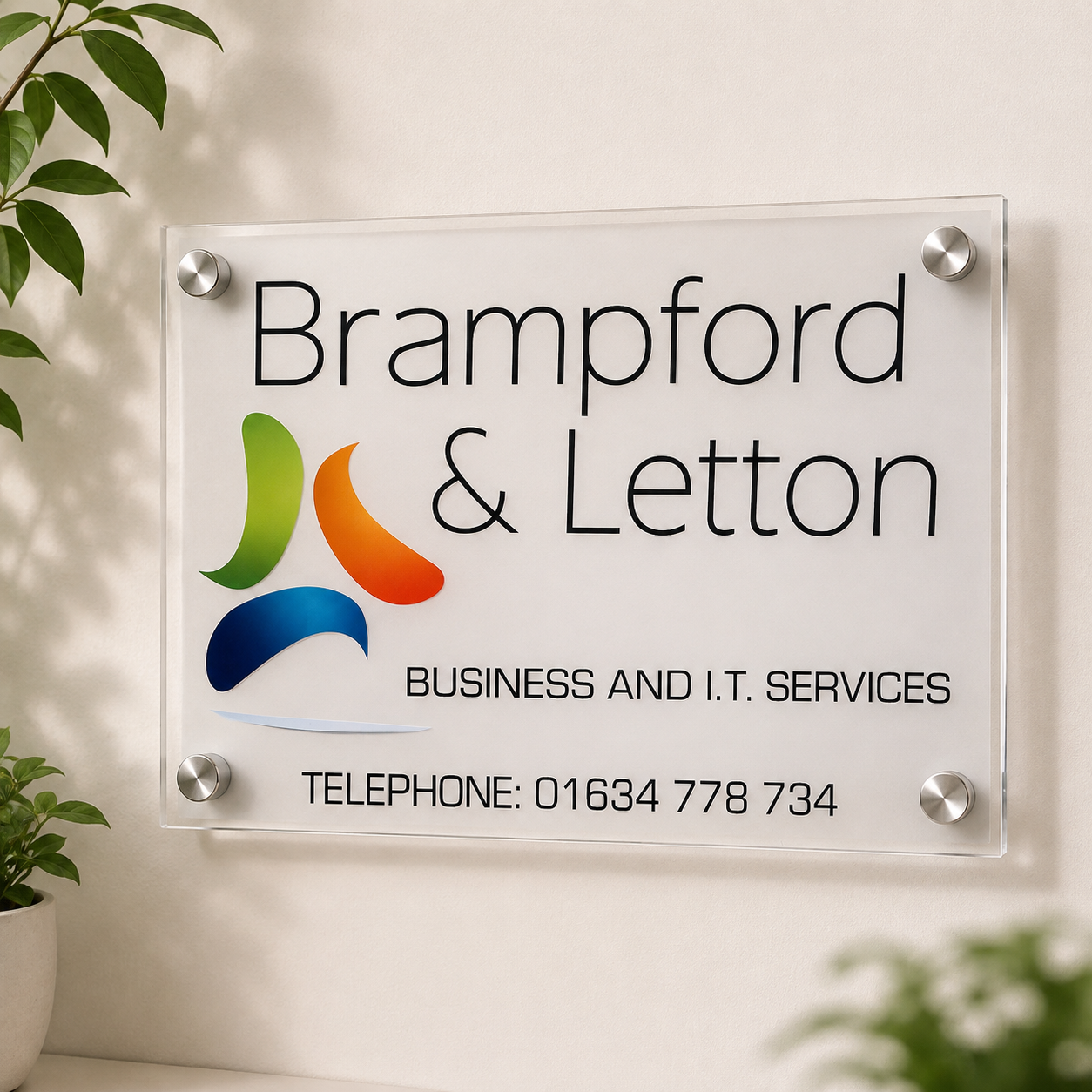 A clear acrylic business name sign mounted on a beige wall, featuring the text 'Brampford & Letton' and 'BUSINESS AND I.T.