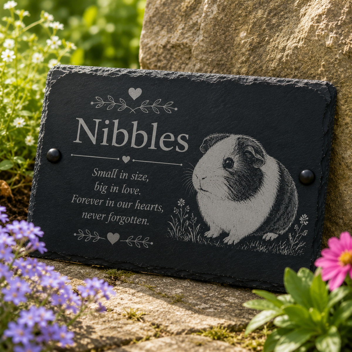 Personalized black slate pet memorial garden plaque engraved with the name 'Nibbles' and a guinea pig illustration, displayed outdoors against a stone wall with flowers in the foreground.