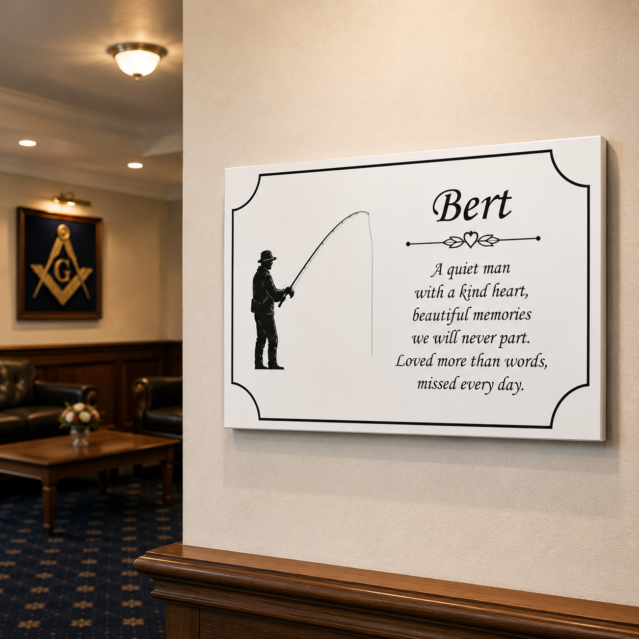 A personalized canvas wall art print hanging on a beige wall in a lobby. The print features a black silhouette of a fisherman on the left and a custom quote on the right that reads: 'Bert - A quiet man with a kind heart, beautiful memories we will never part.