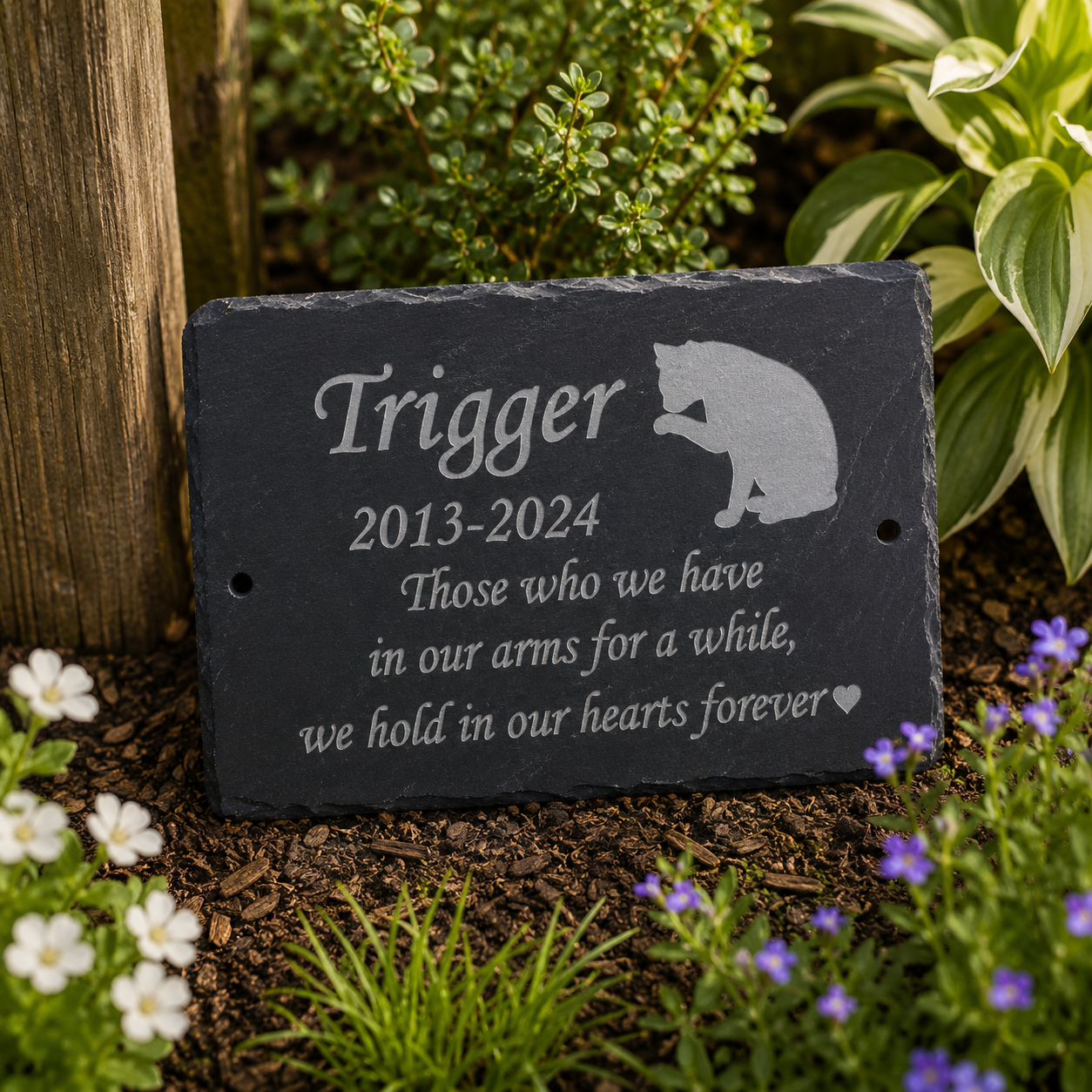 Personalized black slate garden memorial plaque engraved with a cat silhouette and the name 'Trigger 2013-2024' with remembrance text, displayed in a garden setting.