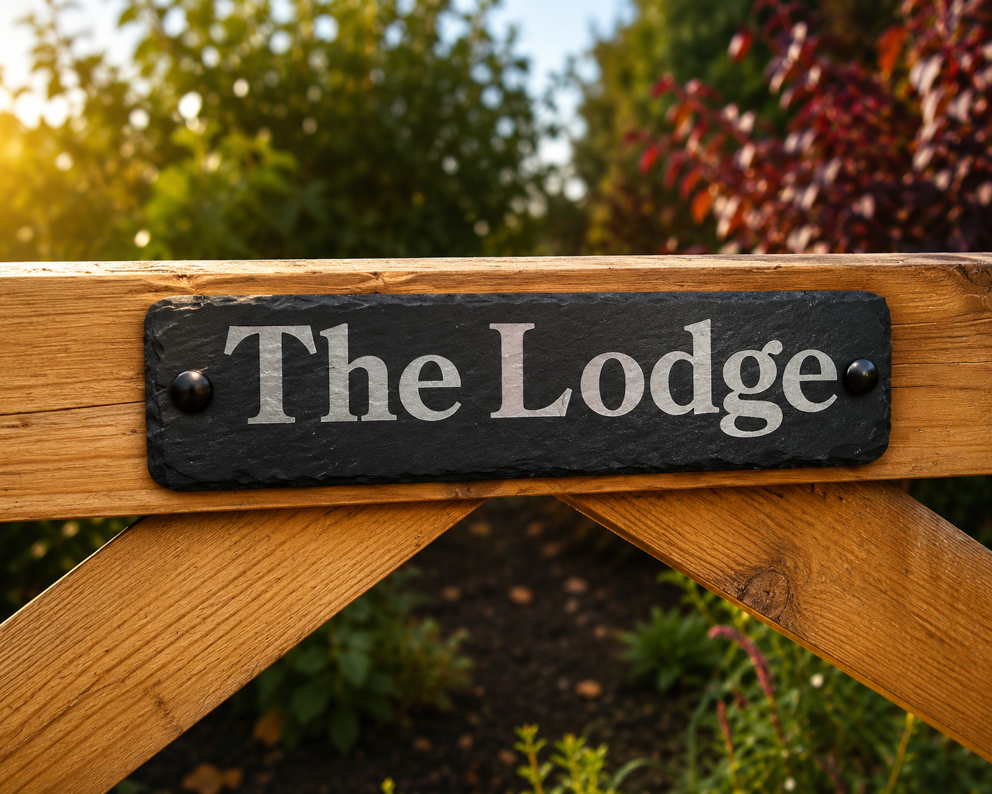 A rectangular black slate sign with white lettering reading 'The Lodge' mounted on a warm golden-brown wooden gate, with a blurred garden background.