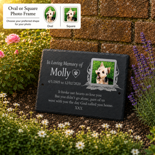 Personalized black slate memorial garden plaque with engraved text and a photo frame holding a small dog portrait, displayed outdoors among flowers and greenery beside a brick wall. A small inset at top left shows oval and square photo frame options.