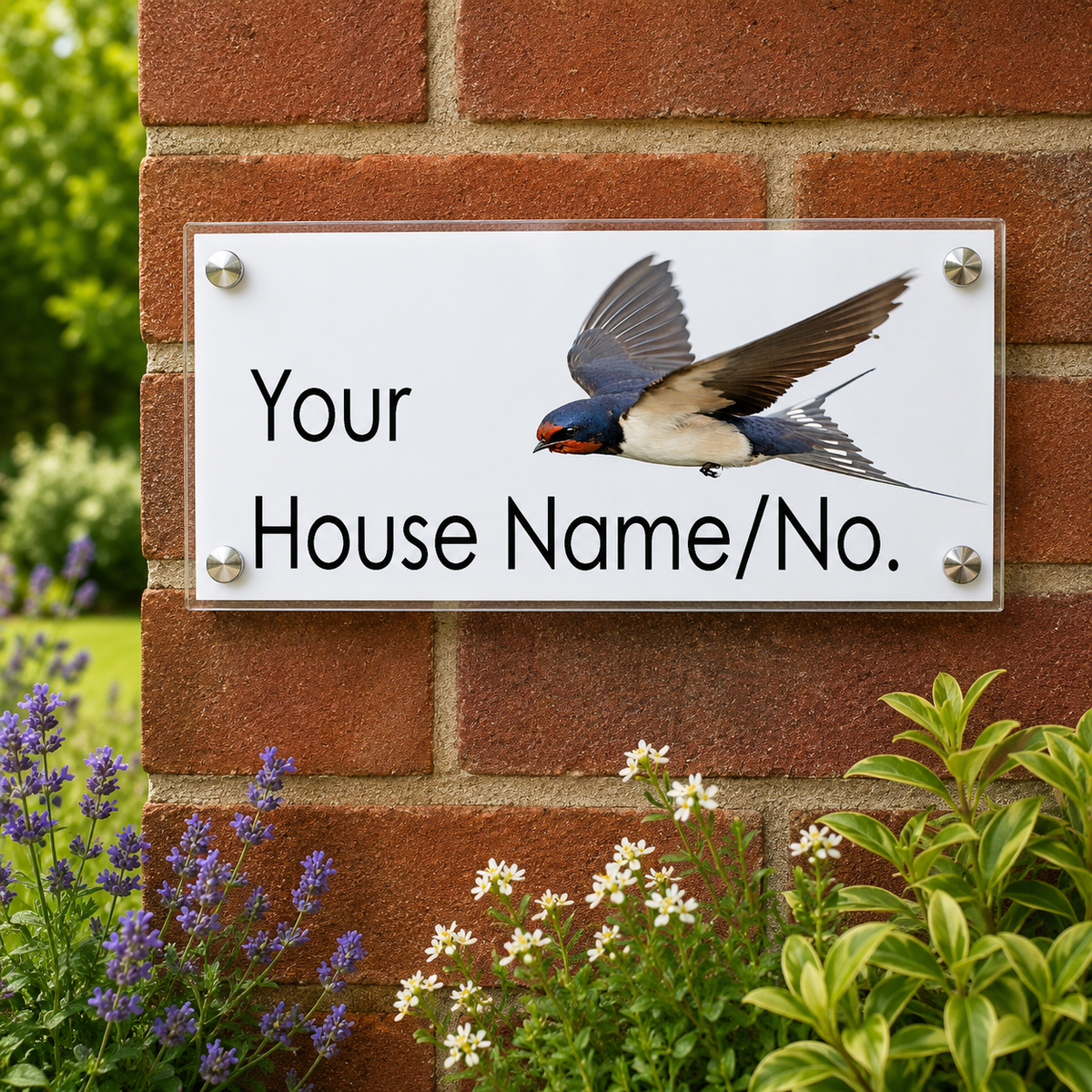 A custom rectangular white house name sign with a photo of a swallow bird and the text 'Your House Name/No.' mounted on a red brick wall with garden plants around it.