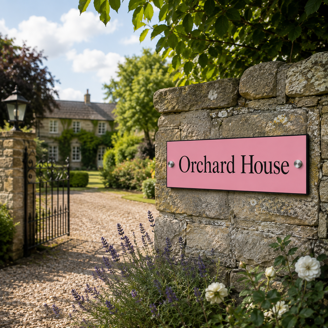 A pink rectangular sign with black text reading 'Orchard House' mounted on a rustic stone wall beside a gravel driveway and garden entrance.