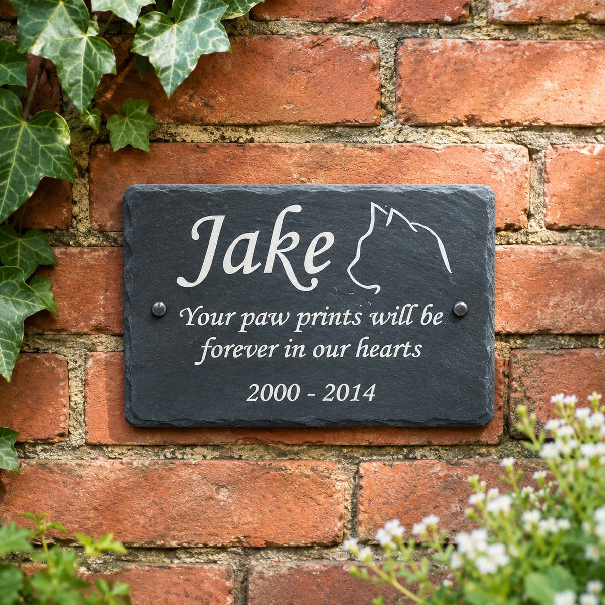 Personalized dark slate pet memorial plaque mounted on a red brick wall, with white engraved text reading 'Jake', 'Your paw prints will be forever in our hearts', and '2000 - 2014'.