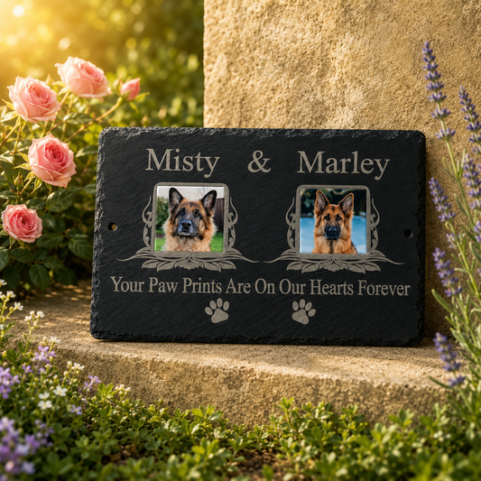 Personalized black slate pet memorial plaque with photos of two German Shepherd dogs and the text 'Misty & Marley' and 'Your Paw Prints Are On Our Hearts Forever,' displayed outdoors on a stone surface with roses and lavender flowers around it.