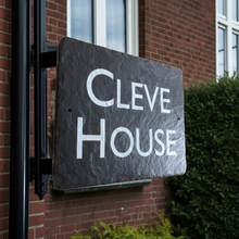 Slate sign with 'CLEVE HOUSE' text on a brick building, held by iron railing