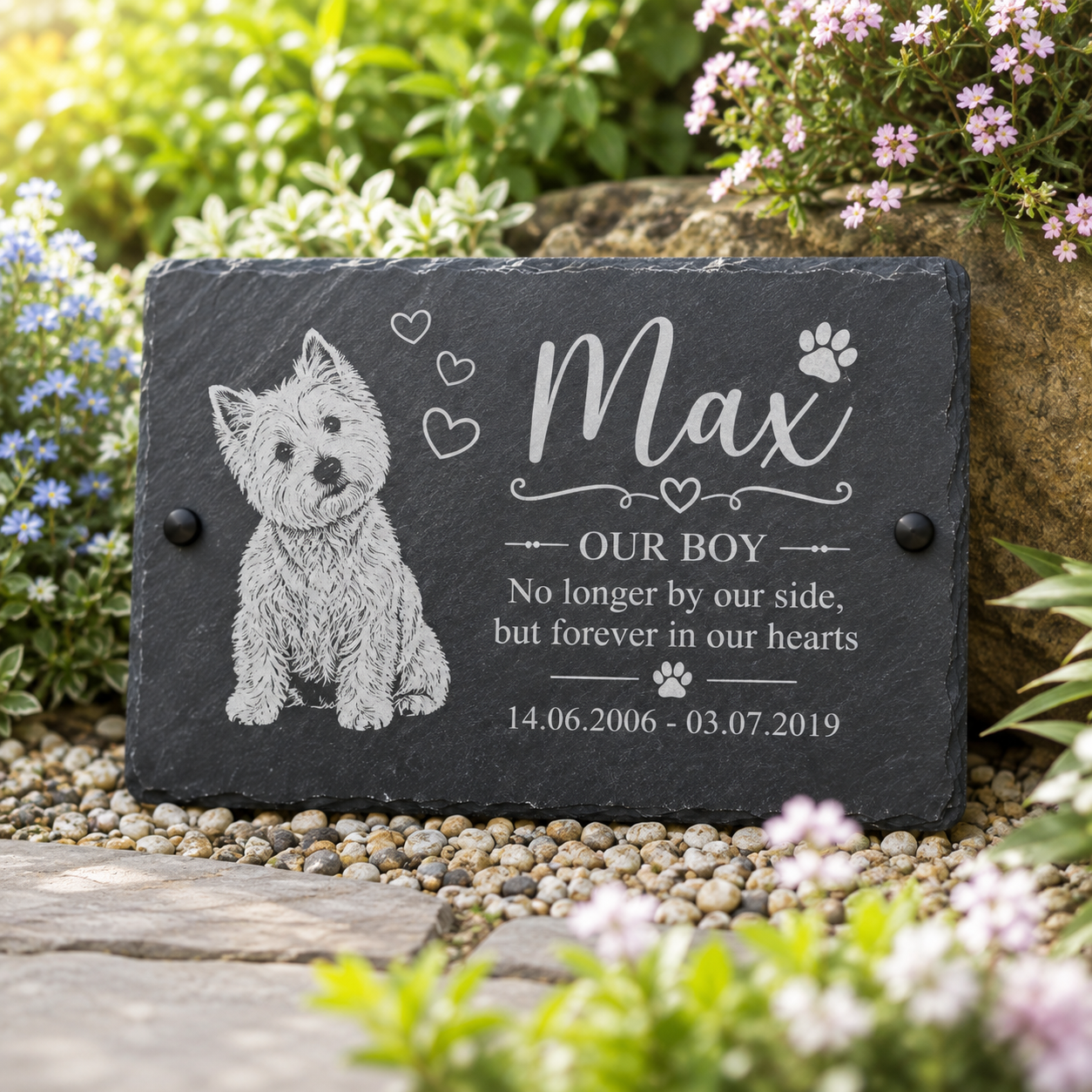Personalized dark slate pet memorial plaque engraved with a West Highland terrier illustration, the name Max, and remembrance text, displayed outdoors on a garden path with flowers and greenery.