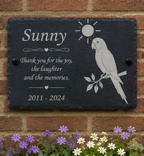 Slate plaque with parrot illustration and text on a brick wall with flowers at the base.