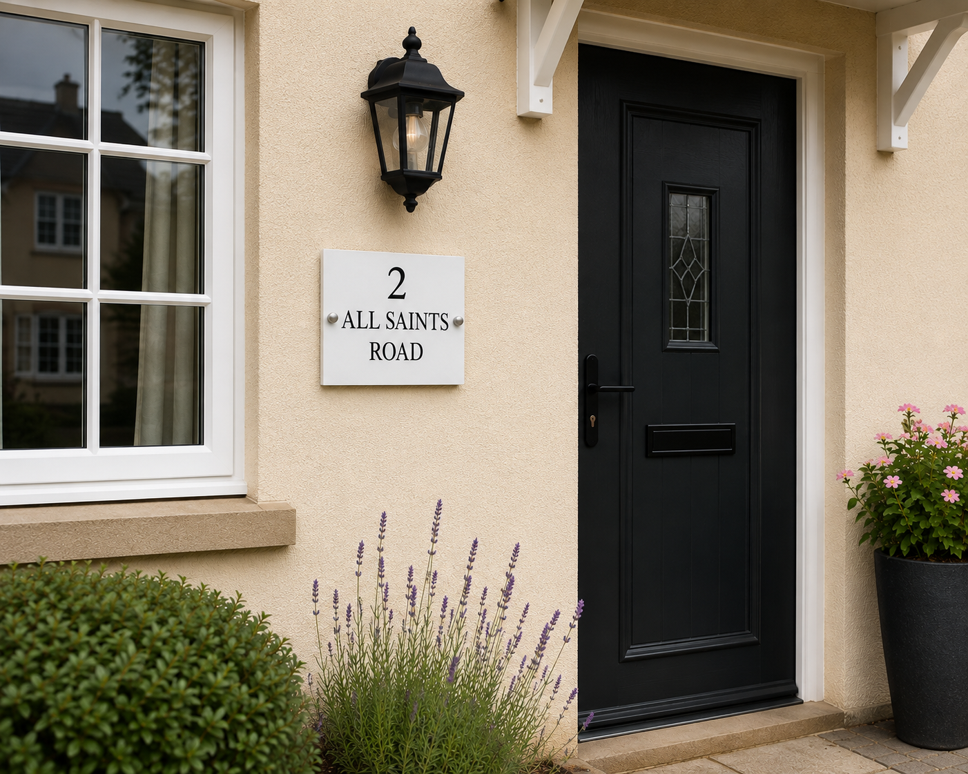 A modern black front door with a small glass window, set in a beige stucco house. A white square house number plaque reading '2 ALL SAINTS ROAD' is mounted on the wall beneath a black outdoor wall lamp.