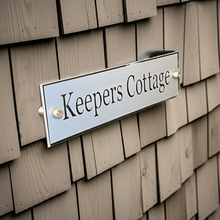 Metal sign reading 'Keepers Cottage' on a wooden wall.
