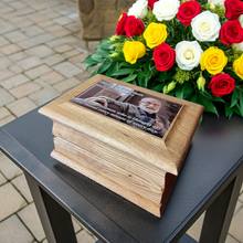 Wooden ashes box with a photo of an elderly man on top, next to a bouquet of flowers.