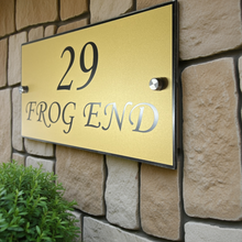 Gold house number sign with '29 FROG END' on a stone wall.