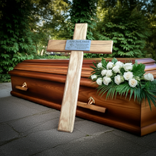 Wooden coffin with a cross and white flowers in front of greenery
