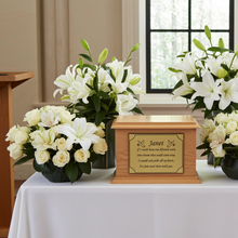 Wooden urn with engraved text on a table with floral arrangements.