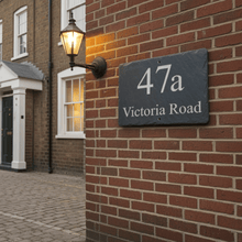 House number 47a Victoria Road on a brick wall with a street lamp in the background.