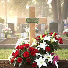 Wreath of red and white flowers with a wooden cross at a cemetery.