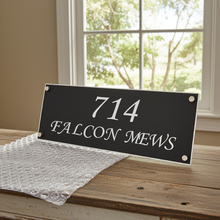 House number sign '714 Falcon Mews' on a wooden surface with bubble wrap, window in the background