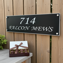 House number sign '714 FALCON MEWS' on a wooden background with a box of chocolates.