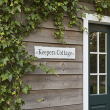 Wooden building with ivy and a sign reading 'Keepers Cottage'.