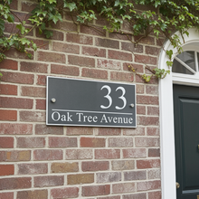 House number sign '33 Oak Tree Avenue' on a brick wall with greenery.