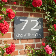 Slate house number sign with '72 King William Close' on a brick wall with red roses.