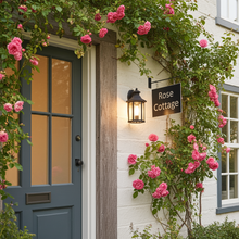 Front door of a house named 'Rose Cottage' with pink flowers and a lamp.