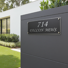Modern house with a gray wall featuring a black address sign displaying '714 Falcon Mews'.